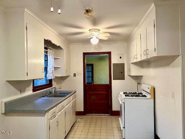 A dated kitchen with white cabinetry, tiled countertops, gas stove, and a red door leading to another room.