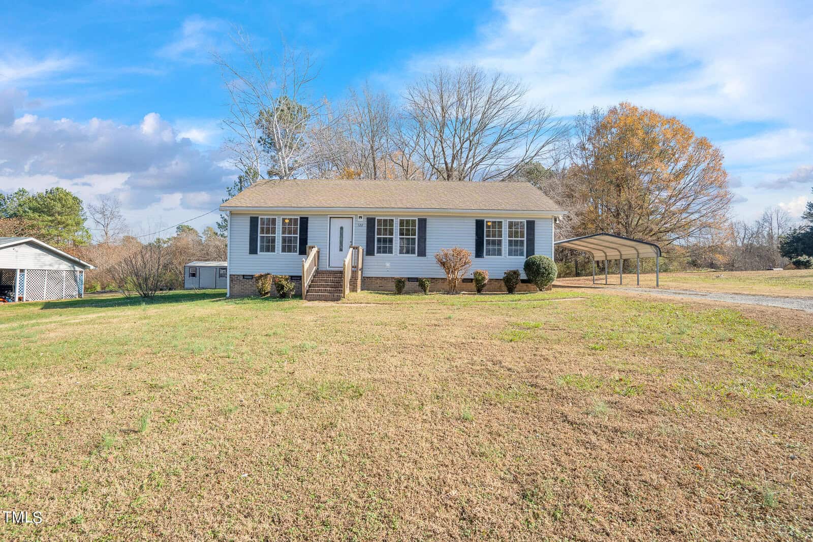 A single-story white house with shuttered windows and a central front door, located at 122 McNair Drive, Henderson NC, is flanked by a small porch. The house is surrounded by a