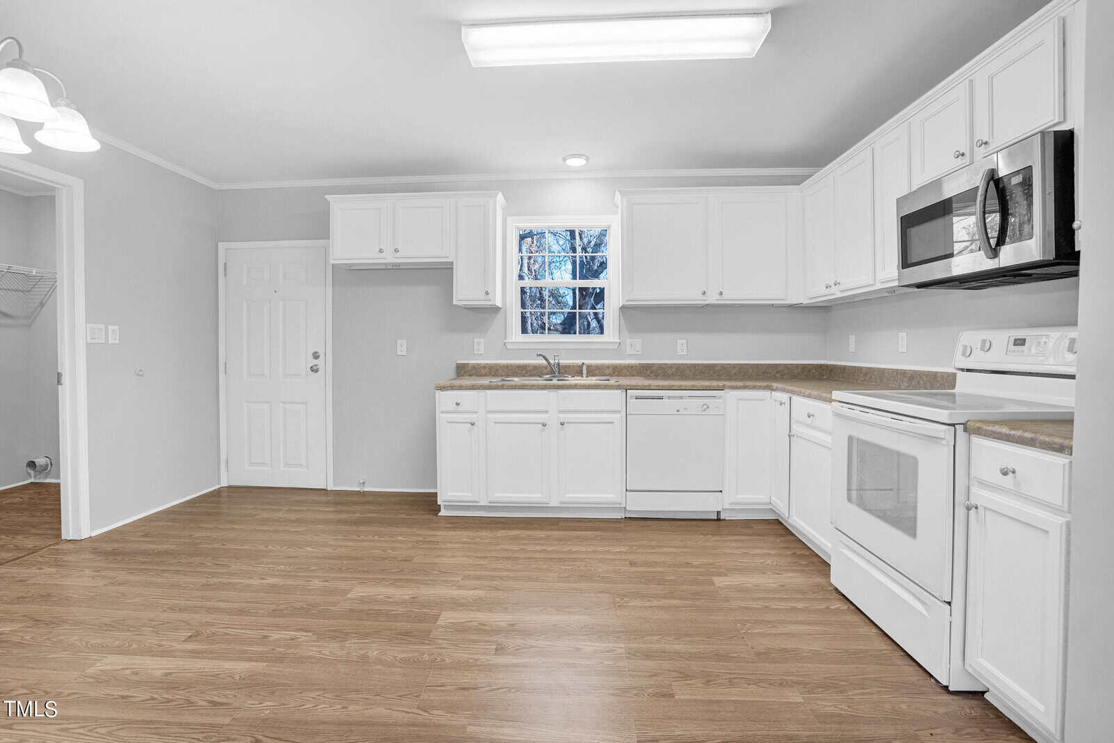 A modern kitchen with white cabinetry, stainless steel appliances, and a granite countertop. the room features wooden flooring and a view of trees through a window.