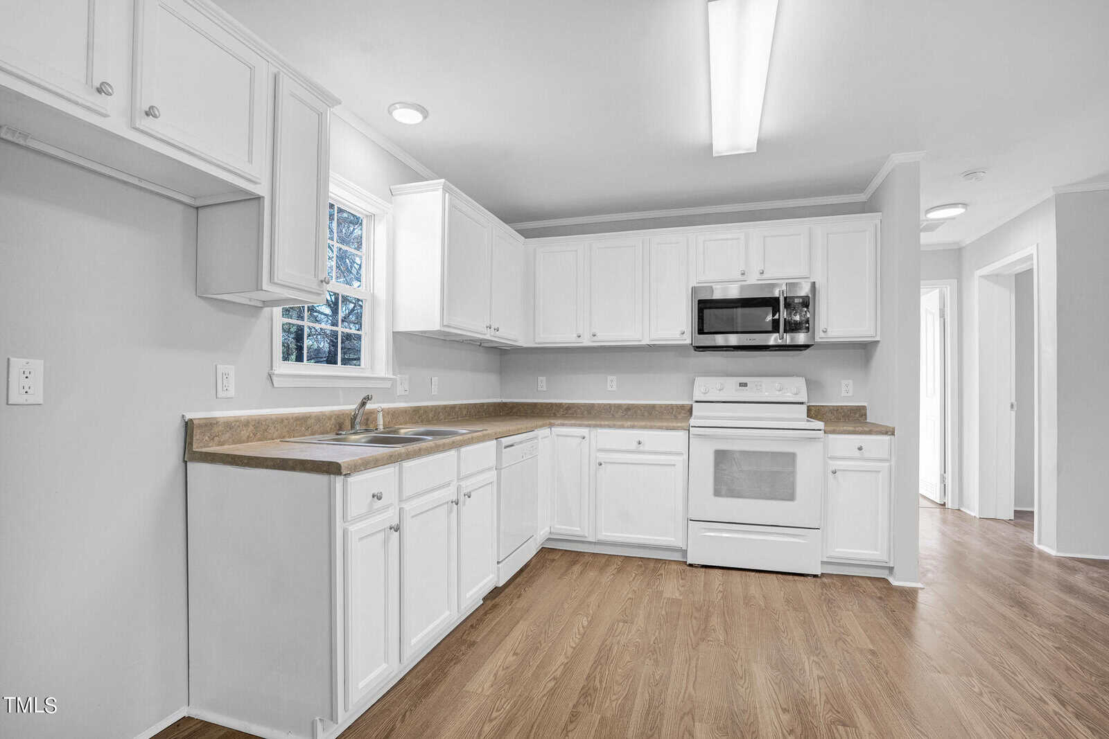 Bright kitchen with white cabinets, granite countertops, and stainless steel appliances. features wood flooring, two windows providing natural light, and a microwave above the stove.