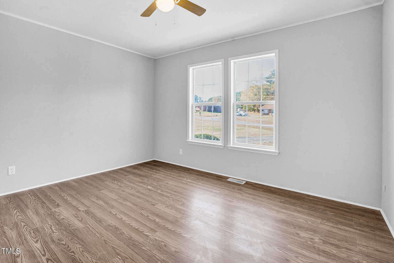 An empty room with light gray walls and laminate flooring featuring a large window with a street view and a ceiling fan.