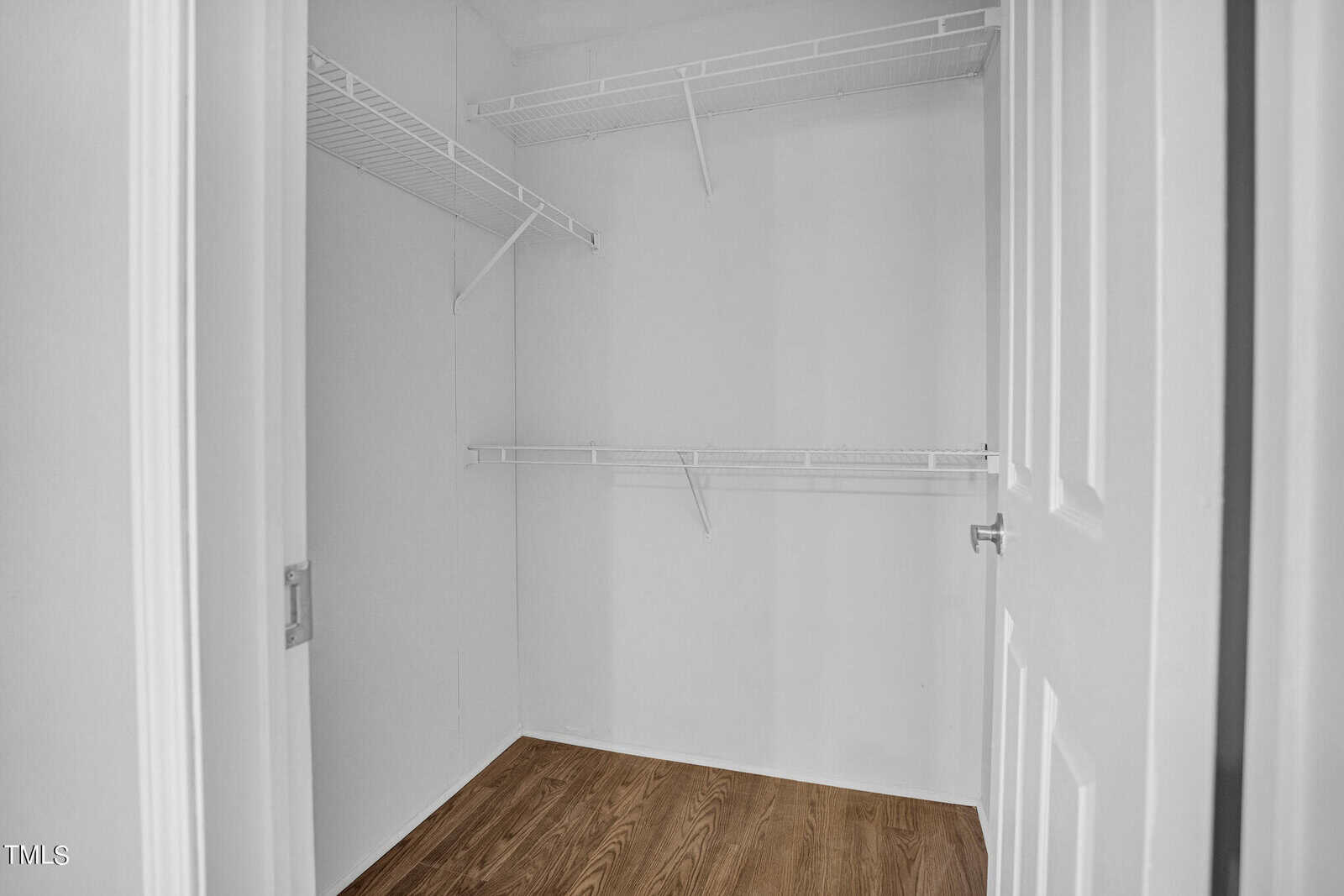 Empty walk-in closet featuring white walls and built-in wire shelving, with a hardwood floor and an open door frame.