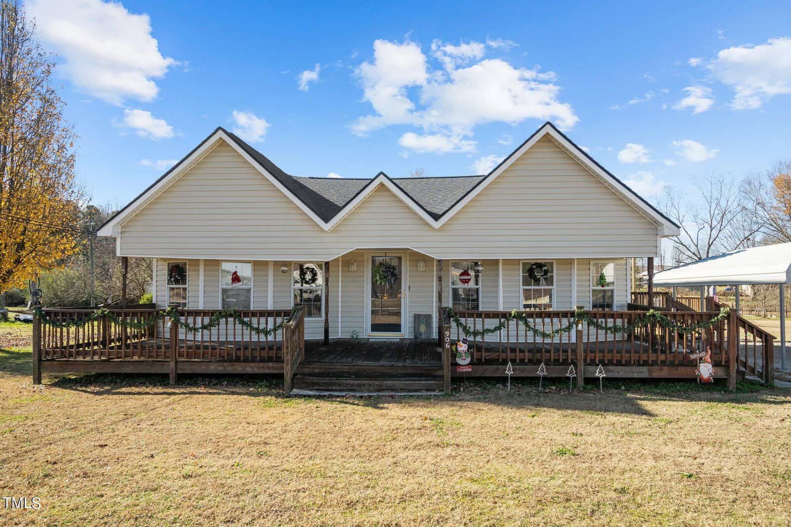 A single-story house with a gabled roof and a large, covered front porch, featuring a wooden railing and christmas decorations.
