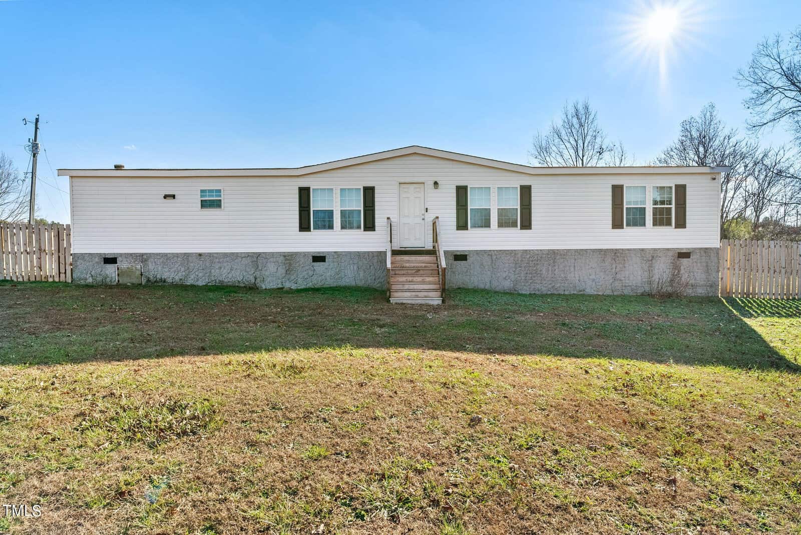 A white single-story manufactured home with a small wooden staircase, situated on a grassy plot at 264 Foxfire Drive, Henderson NC, with a partly cloudy sky overhead.