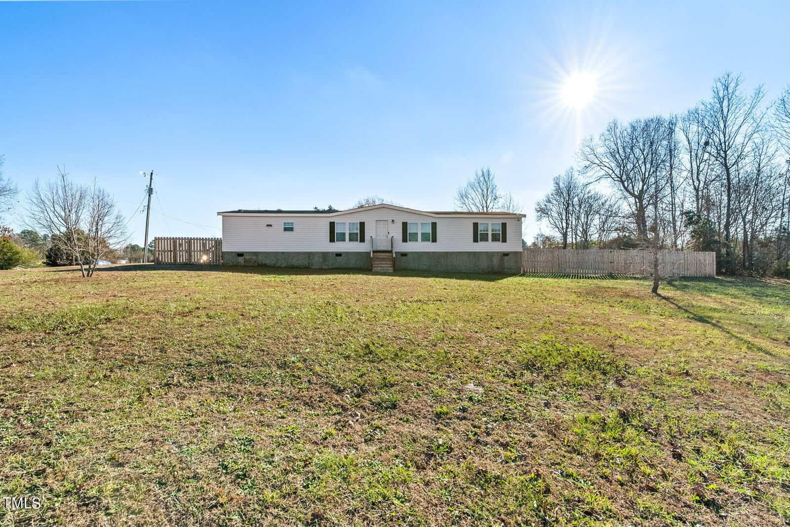 A manufactured home situated on a grassy plot under a clear blue sky with the sun shining brightly.