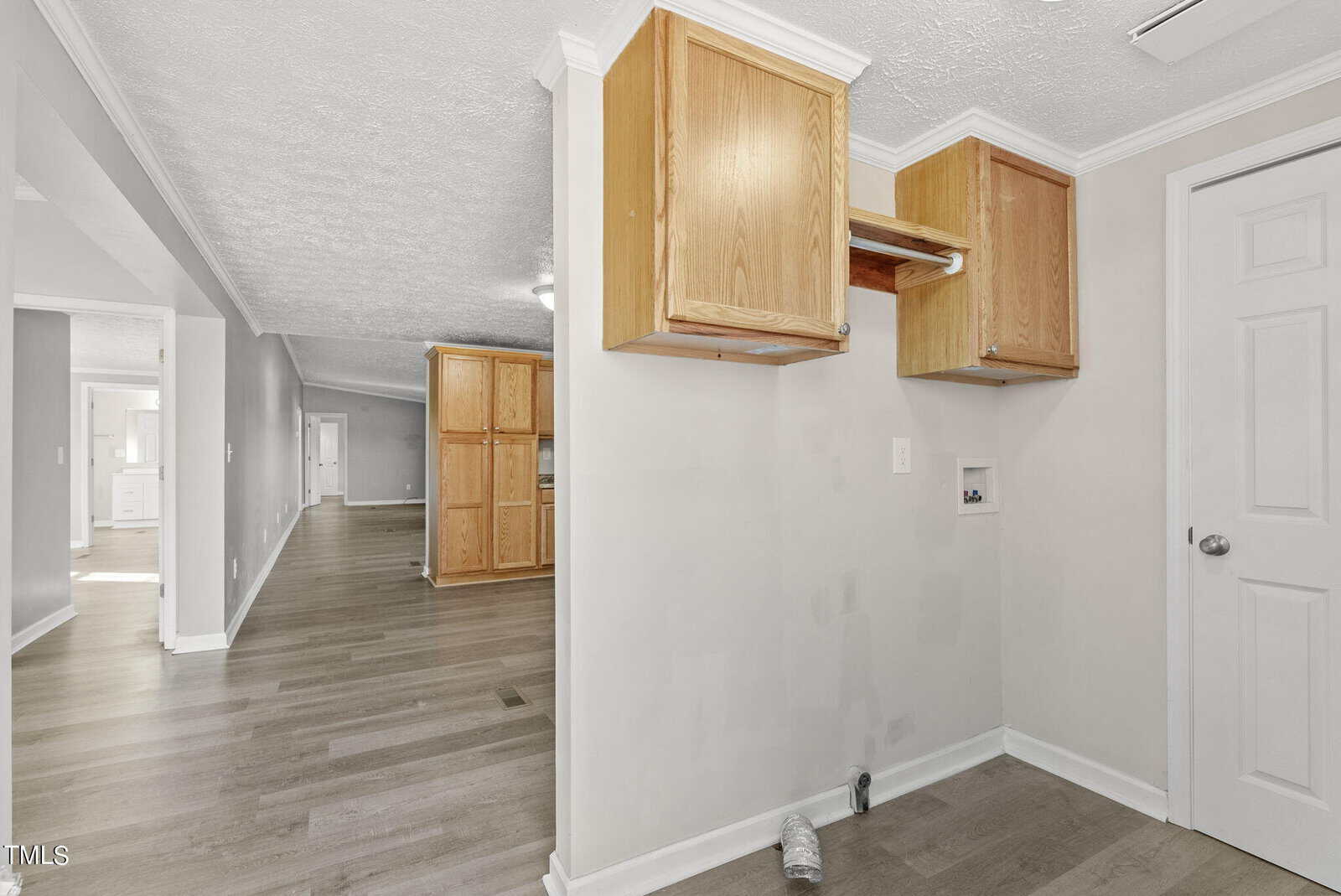 An empty room with wooden cabinetry installed on the wall, laminate flooring, and open doors leading to adjacent rooms.