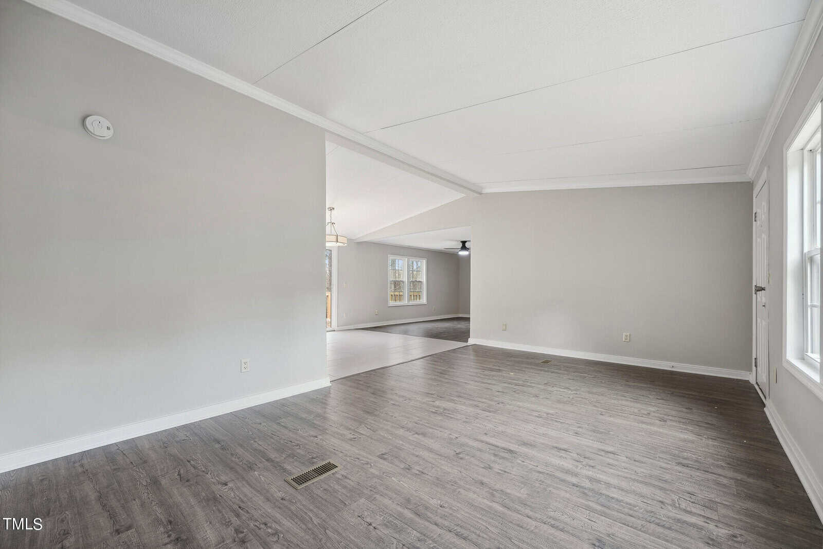 An empty room featuring gray walls, dark wood laminate flooring, and a view into an adjoining room with similar decor.