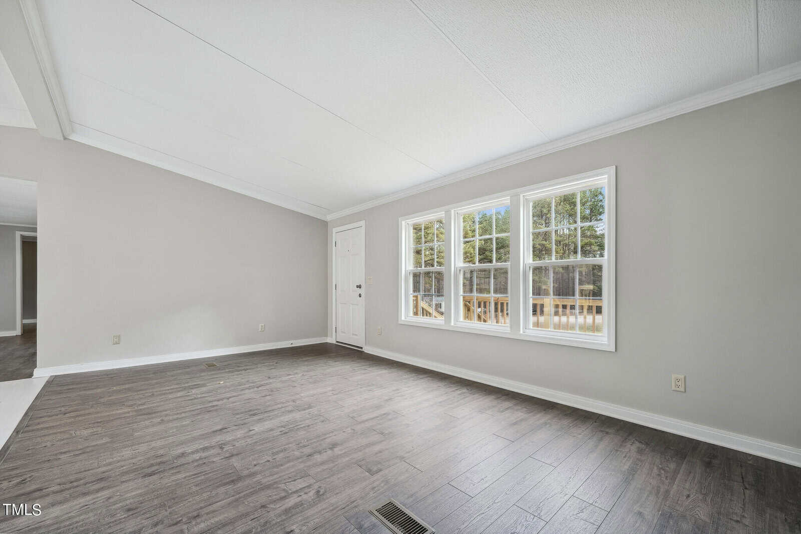 An empty room with light gray walls, dark hardwood flooring, and a large window with a glass door leading to an outdoor deck.