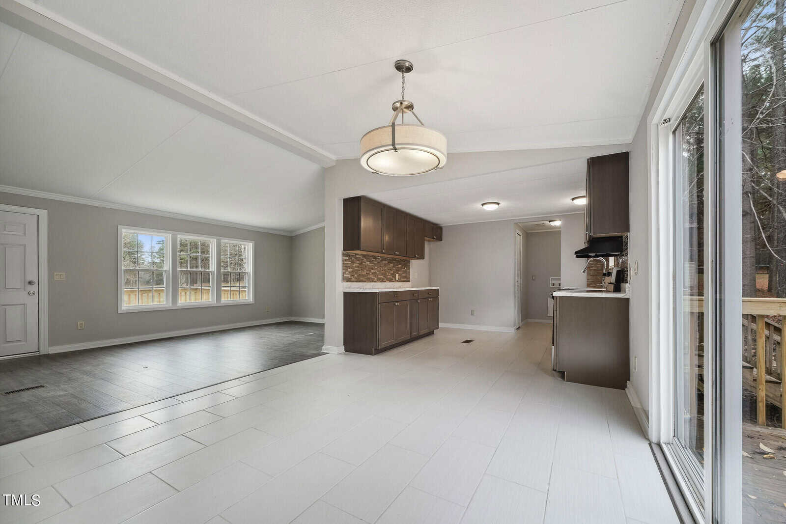 Empty living space with an open floor plan combining a living room and kitchen area, featuring hardwood flooring and a sliding glass door leading to a deck.