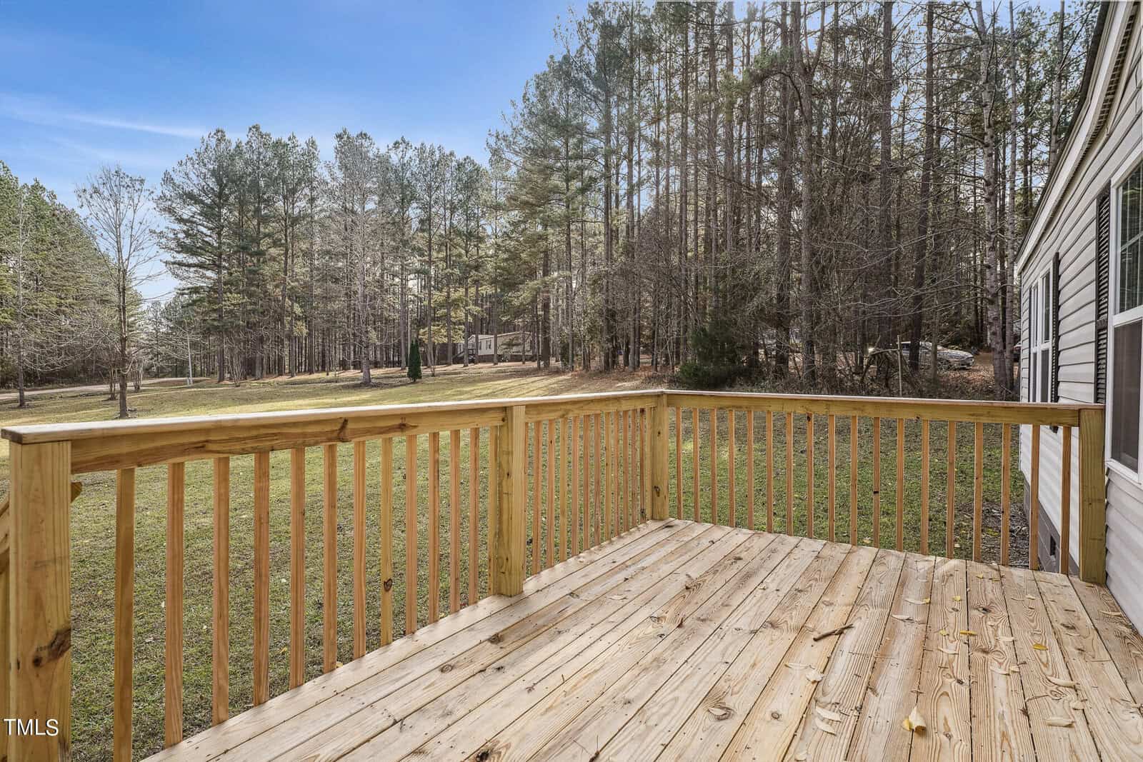 Wooden backyard deck with a view of a grassy area and trees in the distance, clear sky above.