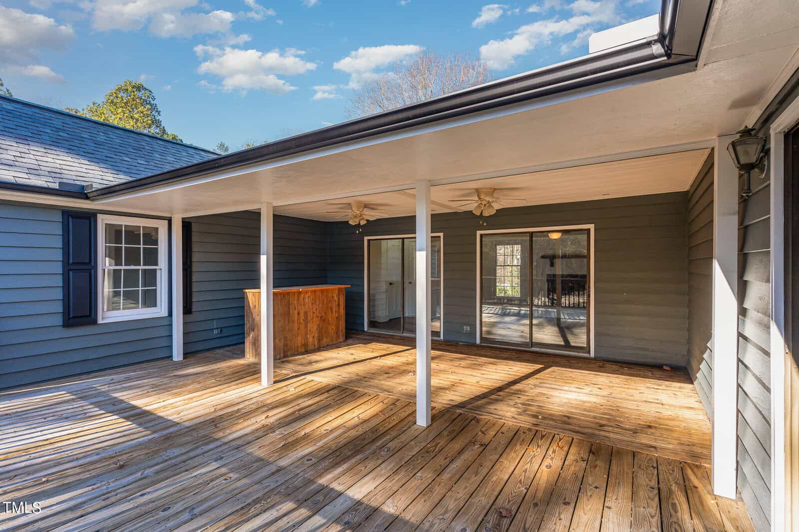 Spacious wooden deck with ceiling fans attached to a house with sliding doors and large windows.