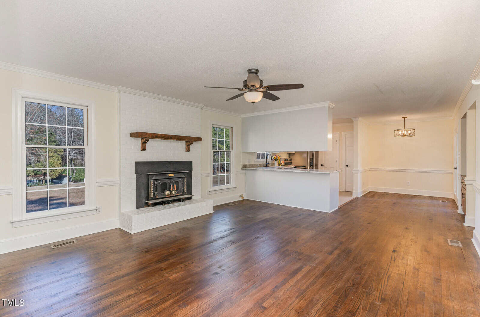 Spacious, well-lit room with a fireplace, hardwood floors, and an open concept layout connecting to a kitchen area.