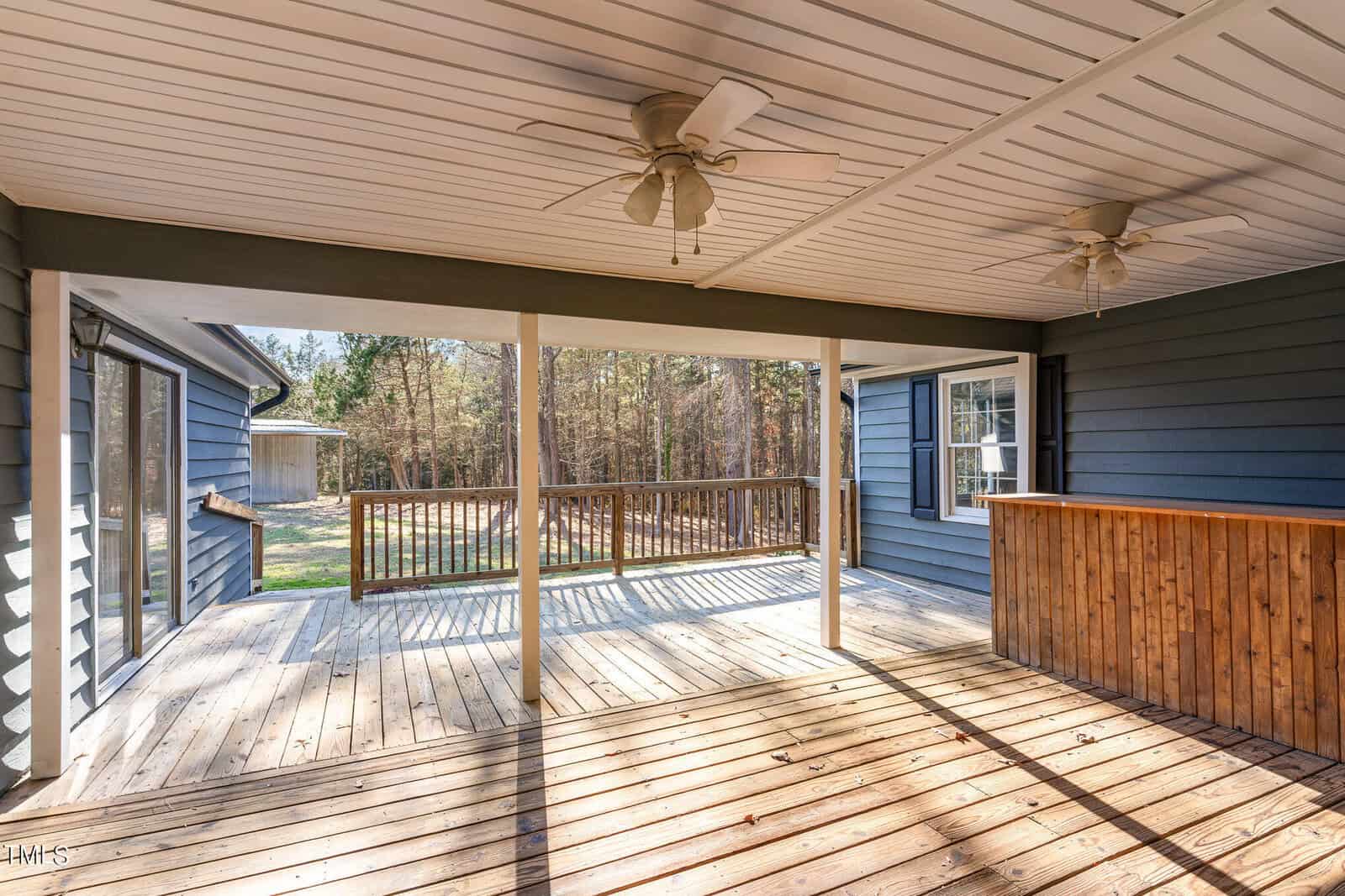 A spacious screened porch with wooden floors, featuring ceiling fans and a view of the adjoining deck and backyard.