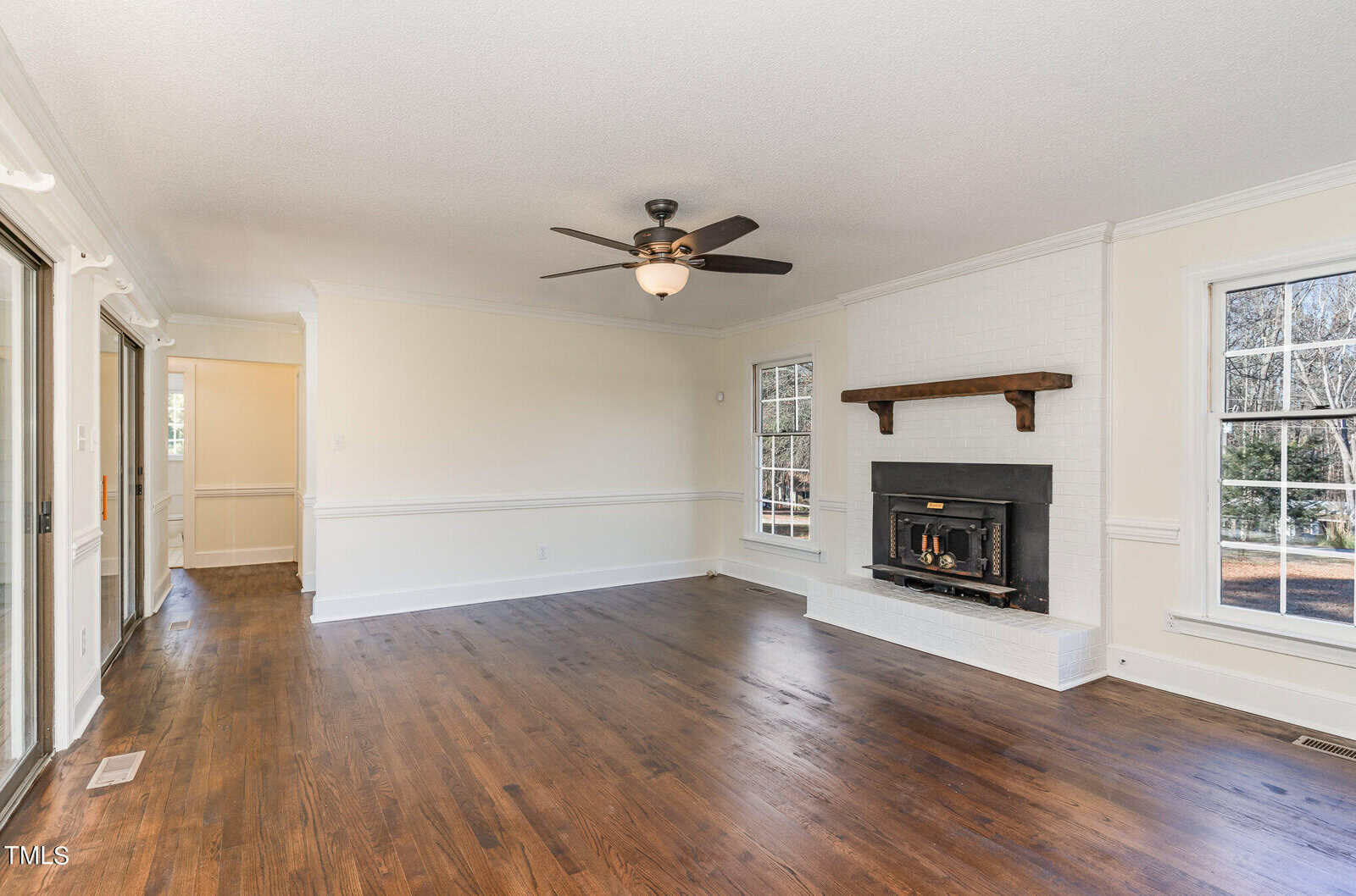 Spacious living room with hardwood flooring, white walls, a fireplace, and a ceiling fan.