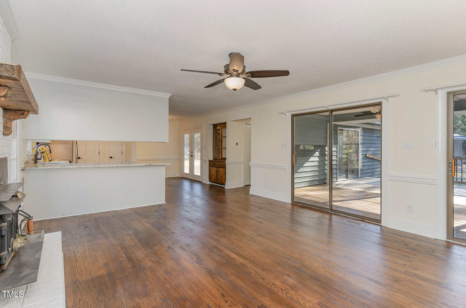 Spacious living room featuring hardwood flooring, a ceiling fan, a fireplace, white walls, and glass doors leading to an adjacent area.