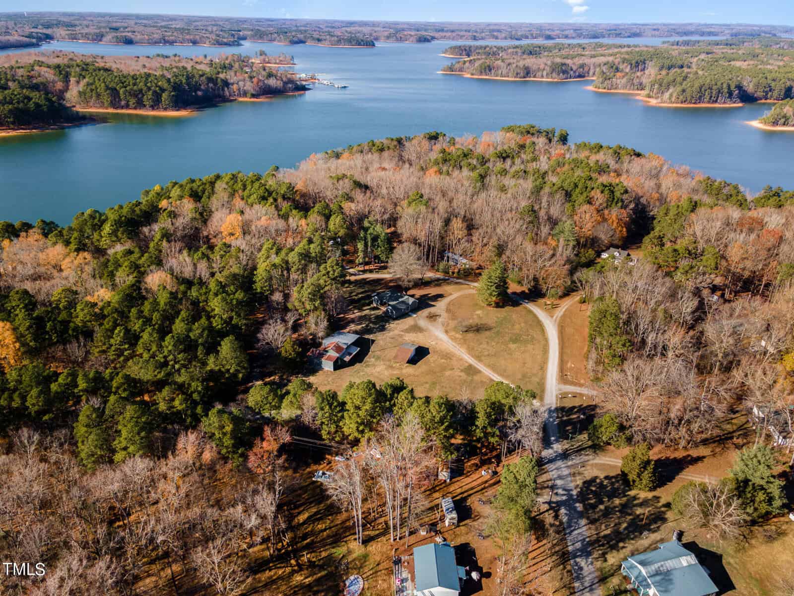 Aerial view of a calm lakeside area with wooded landscape and scattered buildings, connected by a winding path.