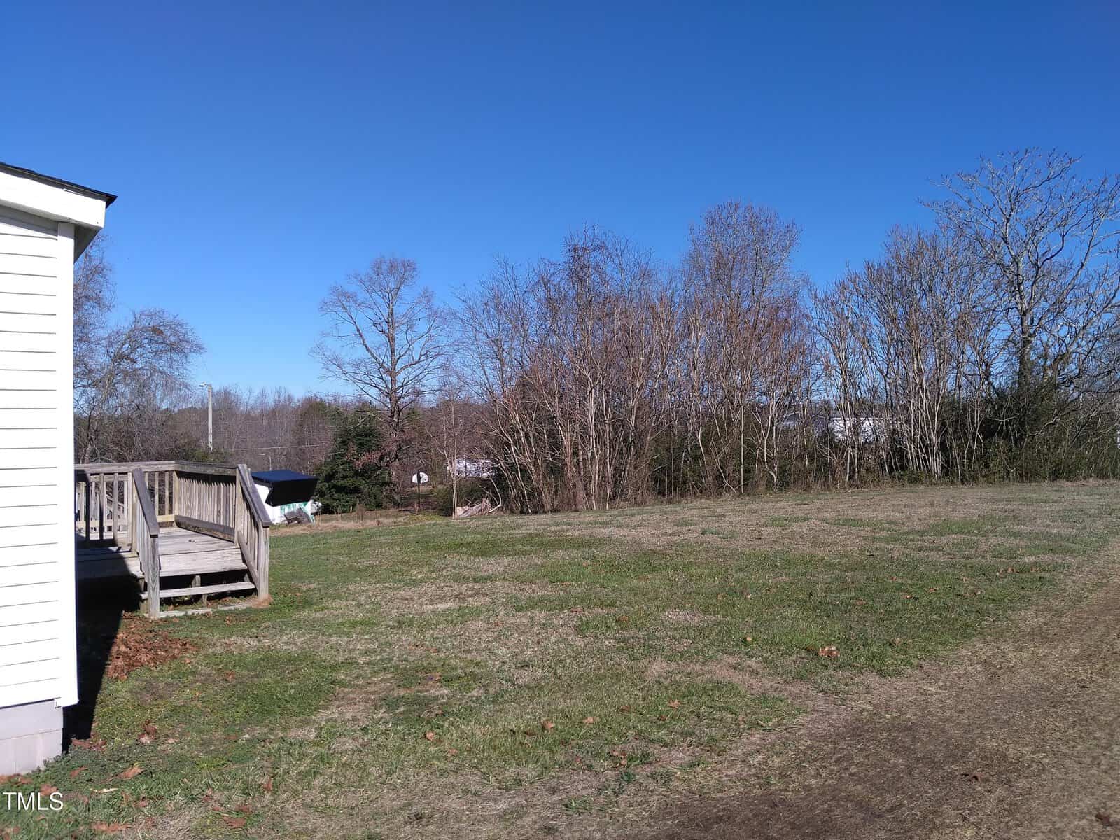 A clear day over a residential backyard with a small wooden deck on the left, bare trees in the background, and a well-worn grass path leading off to the right.