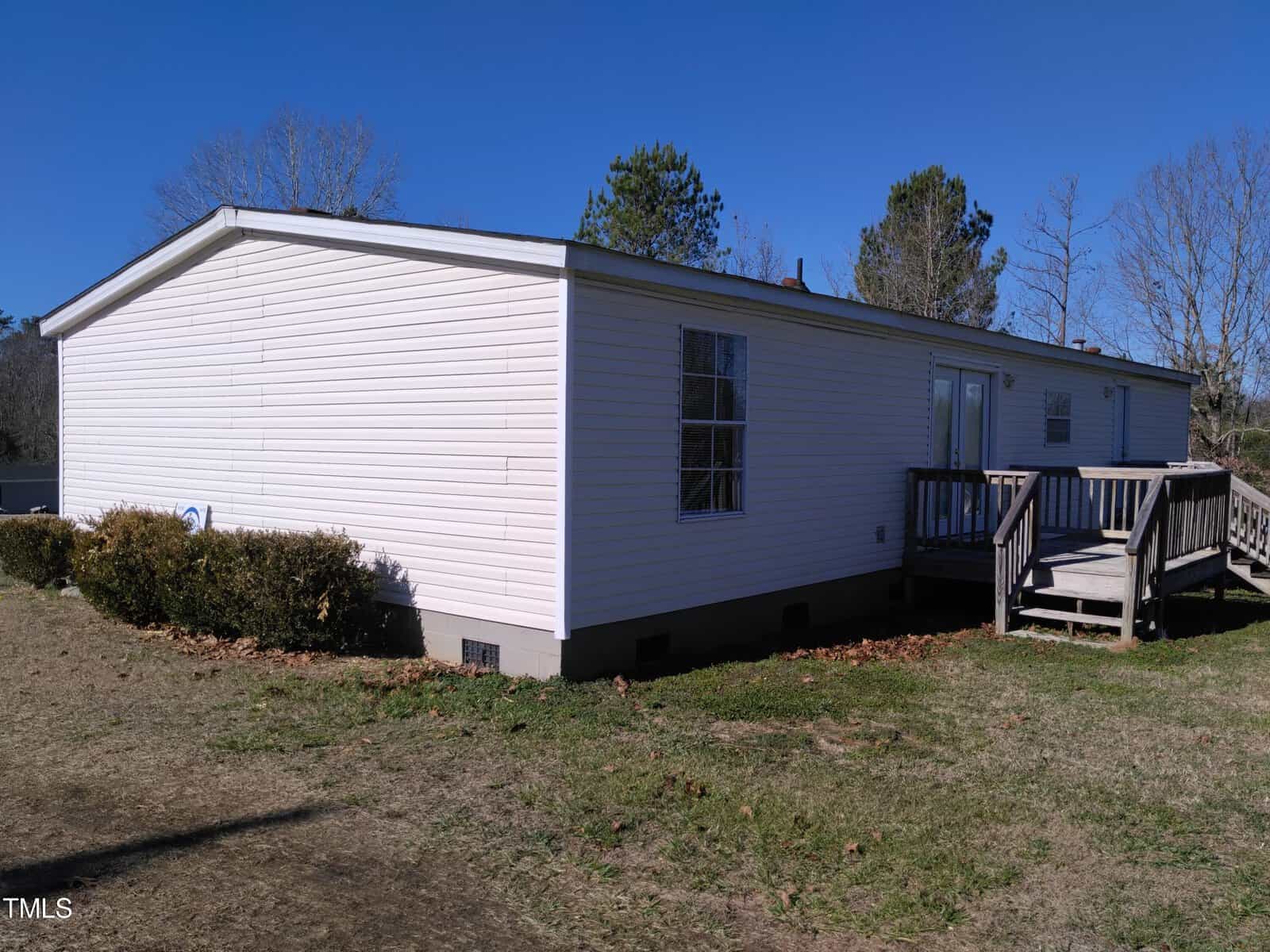 A single-story mobile home with white siding and a small wooden deck under a clear sky.