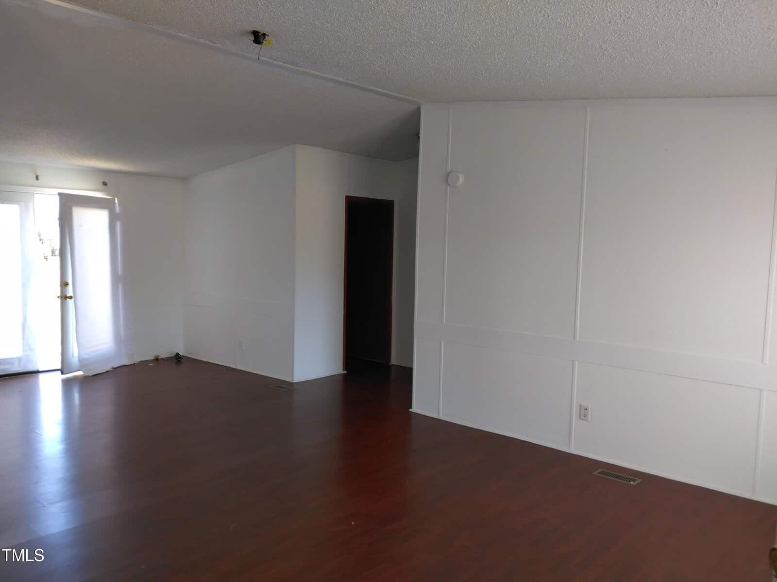 Empty room with wooden flooring, white walls, and a sliding glass door leading to another area.
