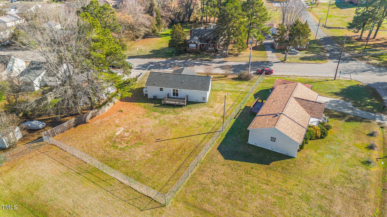 Aerial view of a suburban area showcasing two houses with distinct, large pitched roofs and fenced yards. one house is white; the other features brown shingles. there are trees and a road visible.