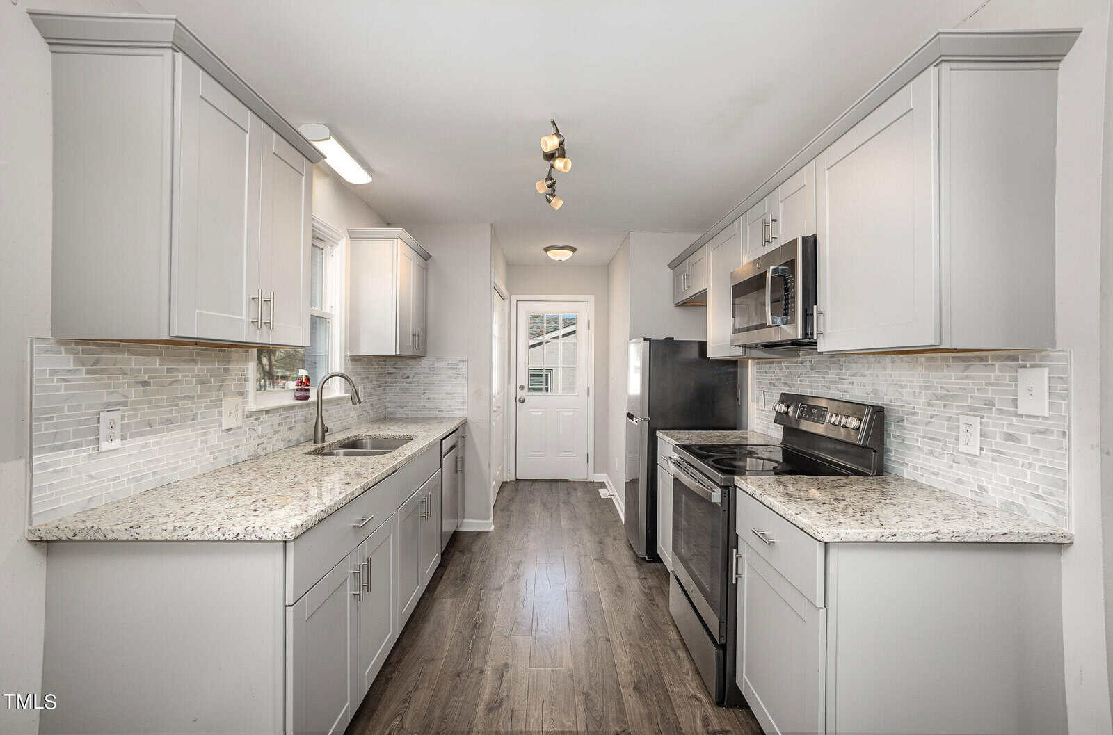 A modern kitchen with gray cabinets, granite countertops, and stainless steel appliances. features a subway tile backsplash and dark wood flooring.