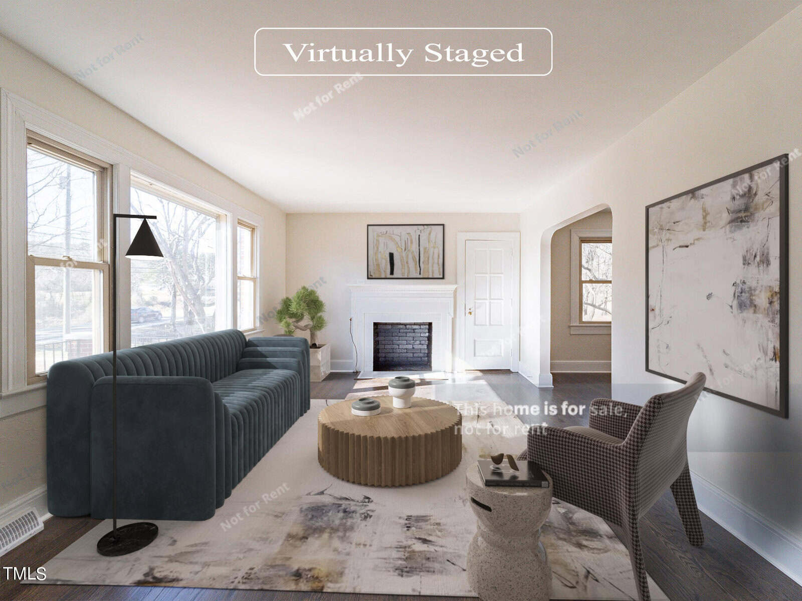 A virtually staged living room features a teal sofa, round coffee table, and modern floor lamp. The white walls and large windows brighten the space. A fireplace is centered on the far wall, and abstract art decorates the room.