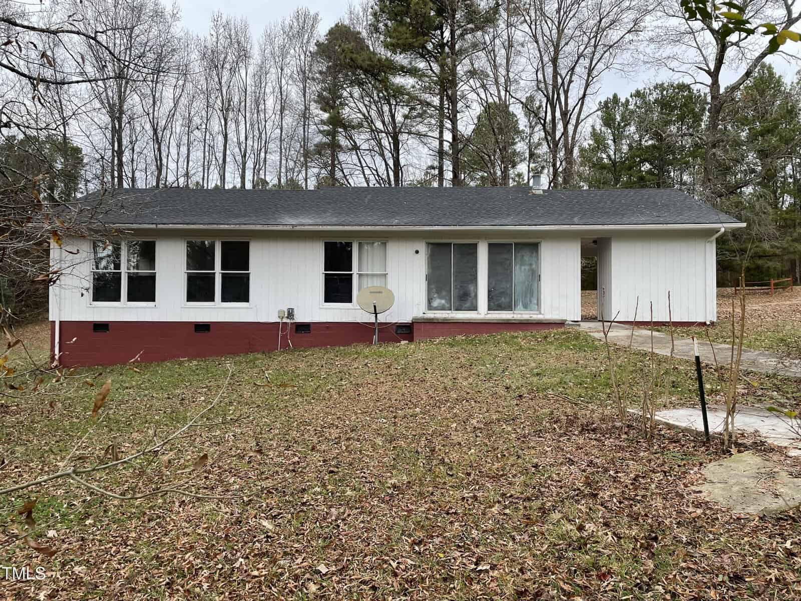 A single-story white house at 1025 Wilson Brothers Road, Henderson NC, with a red base, three front windows, and a basketball hoop to the side, surrounded by a grassy yard with