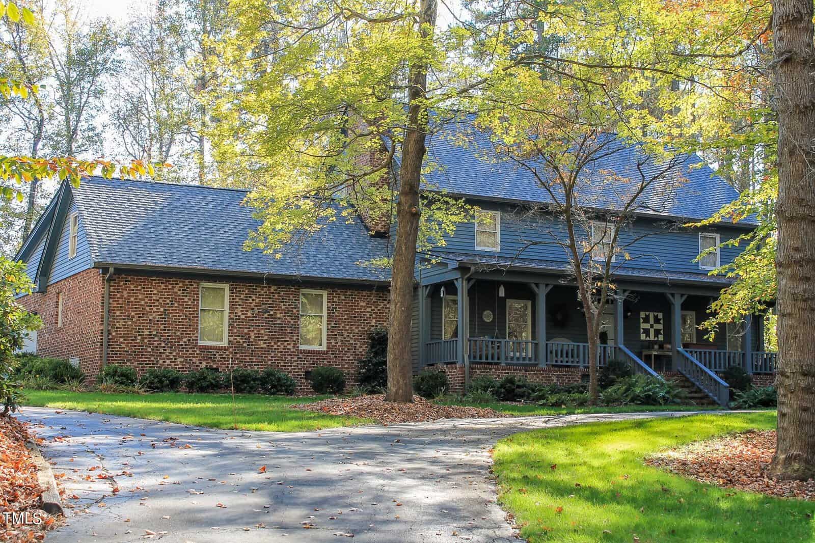 A two-story house with a brick and dark blue siding facade, featuring a front porch and surrounded by trees with autumn foliage.