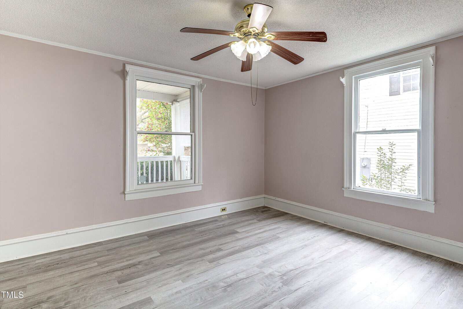 An empty room with light pink walls, grey flooring, two windows, and a ceiling fan.