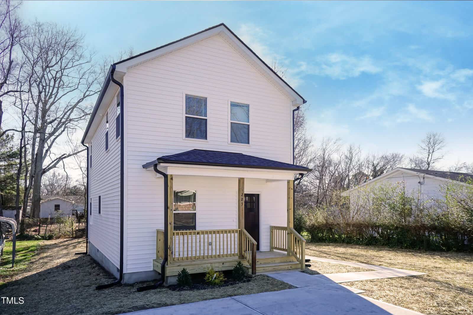 The charming two-story white house at 223 W College Street features a small porch, dark roof, and wooden stairs leading to the front door. Surrounded by a grassy yard and trees under Oxford's clear blue sky, it promises serene living.