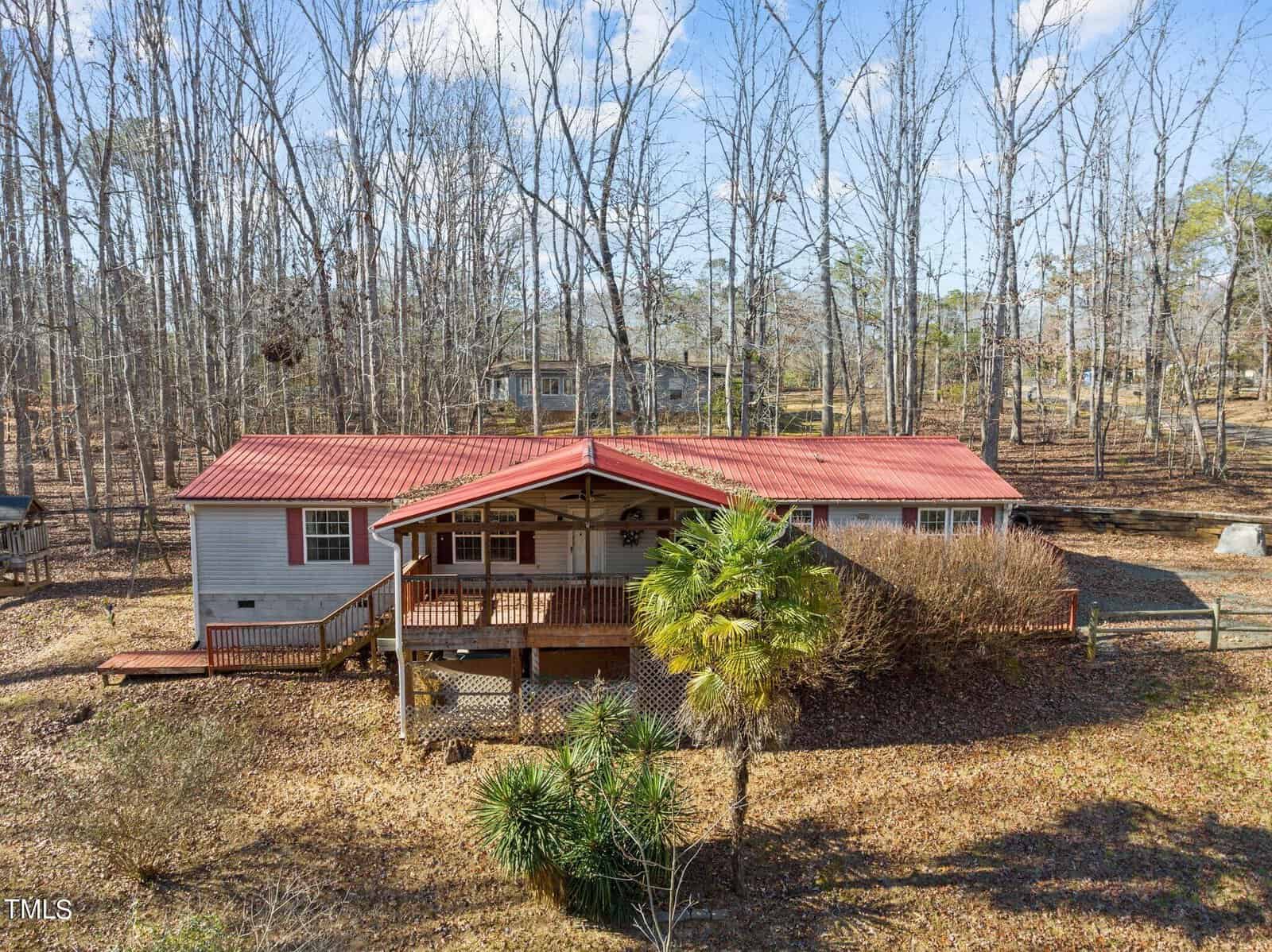 Nestled at 3514 Topaz Street, a cozy house with a red roof and covered porch stands amid bare trees in a wooded area. A palm tree and some shrubbery grace the foreground, while the sky above Wake Forest is partly cloudy.