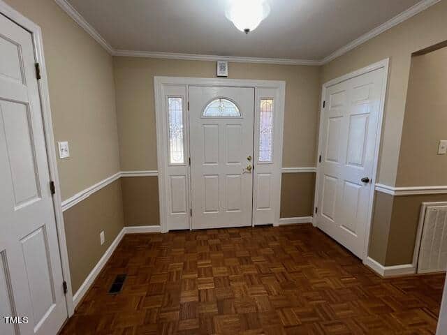 An empty room featuring a parquet floor, a white front door with an arched window, white walls with wainscoting, and multiple closed doors.