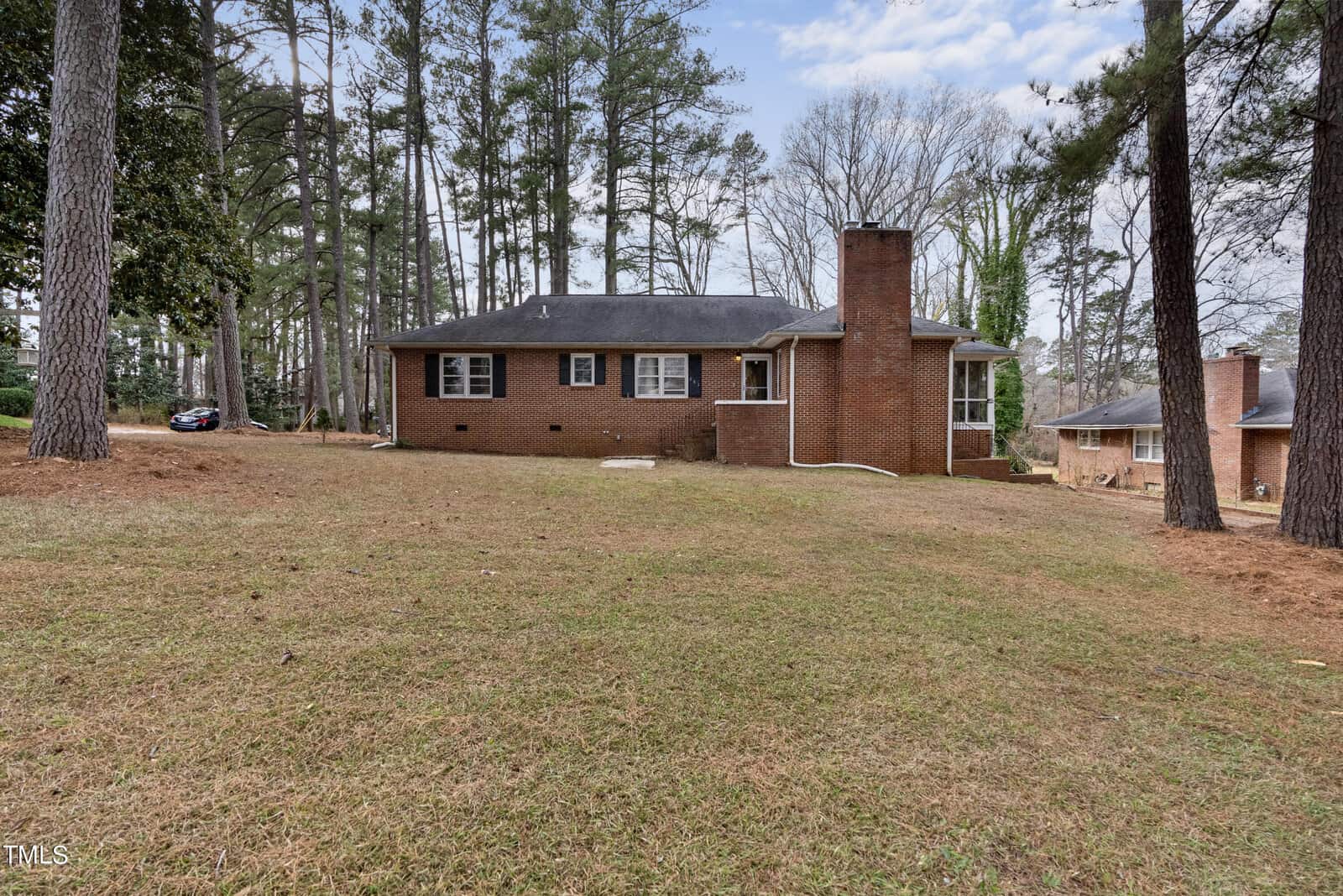 A single-story brick house with a chimney, located at 203 Edgewood Drive, Henderson NC, surrounded by tall pine trees and a lawn in the foreground.