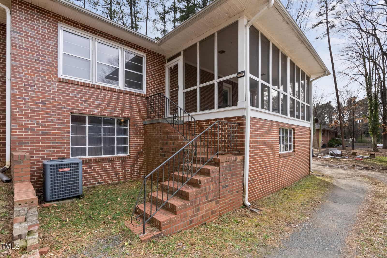 A brick house featuring a screened-in porch and an external staircase leading to the upper level, with a heating and cooling unit visible on the left side.