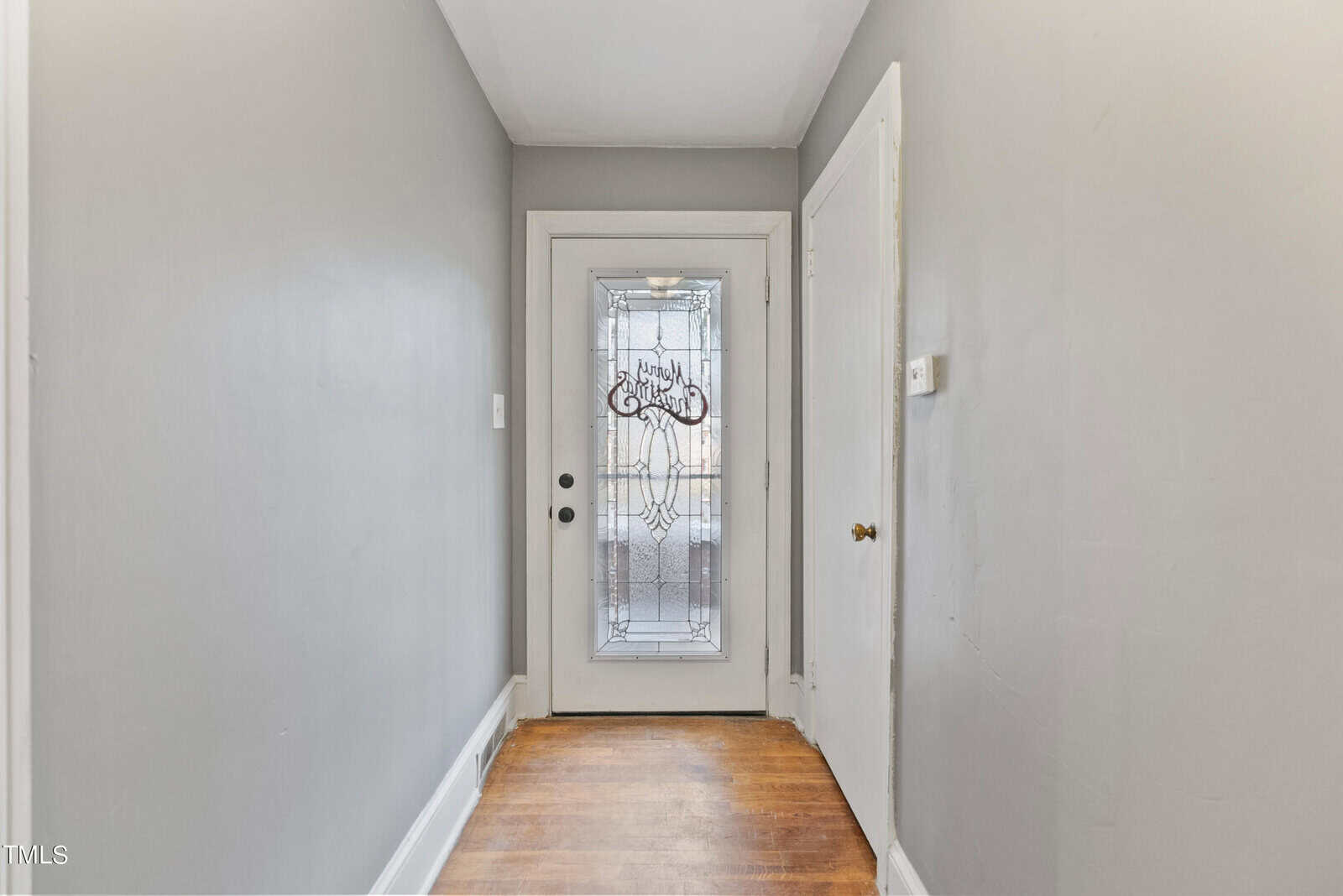 A hallway with hardwood floors leading to a front door with ornamental glass and a sidelight.