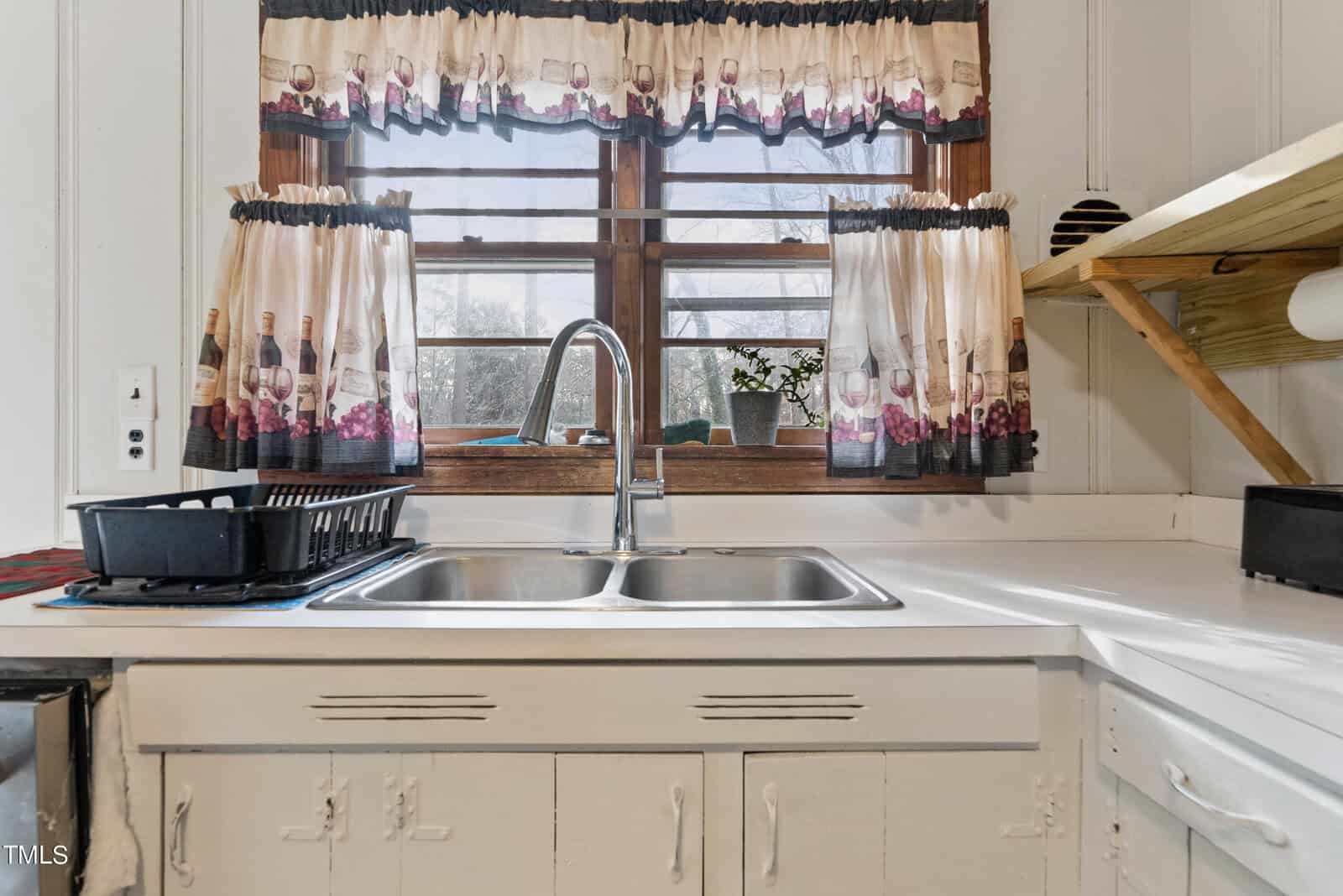 A well-lit kitchen sink with a window, featuring patterned curtains and a drying rack with dishes on the countertop.