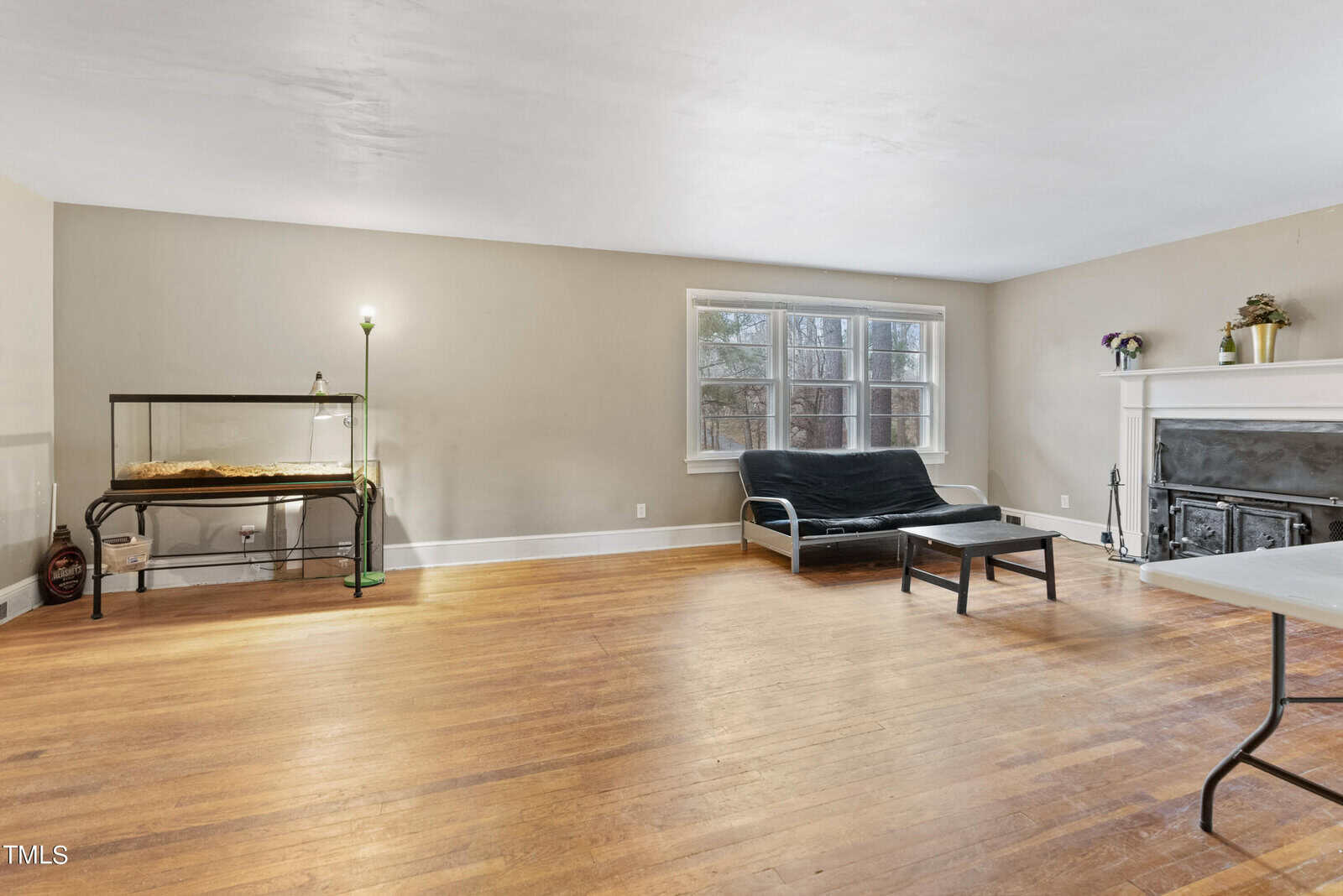 A spacious living room with hardwood floors, featuring a fireplace, a chaise lounge, and a small table with minimal décor.