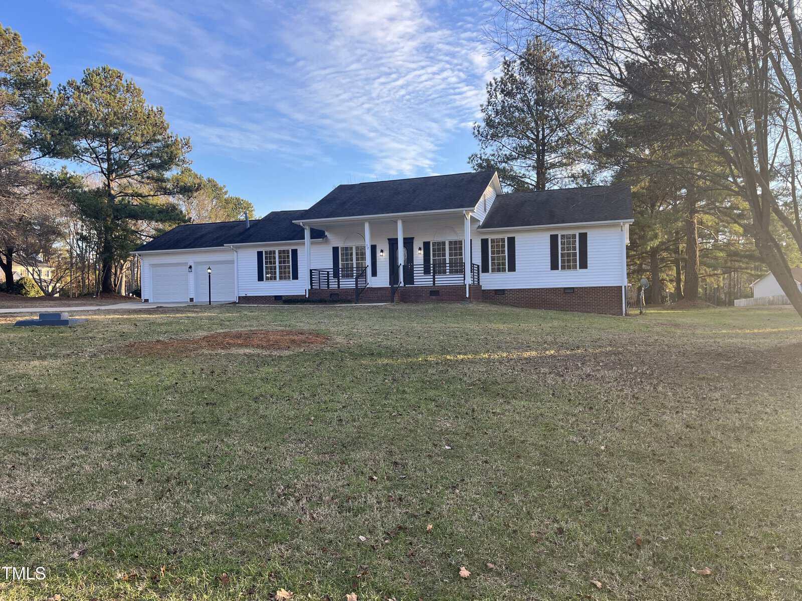 A single-story white house with a porch, surrounded by a grassy lawn and trees under a clear sky.