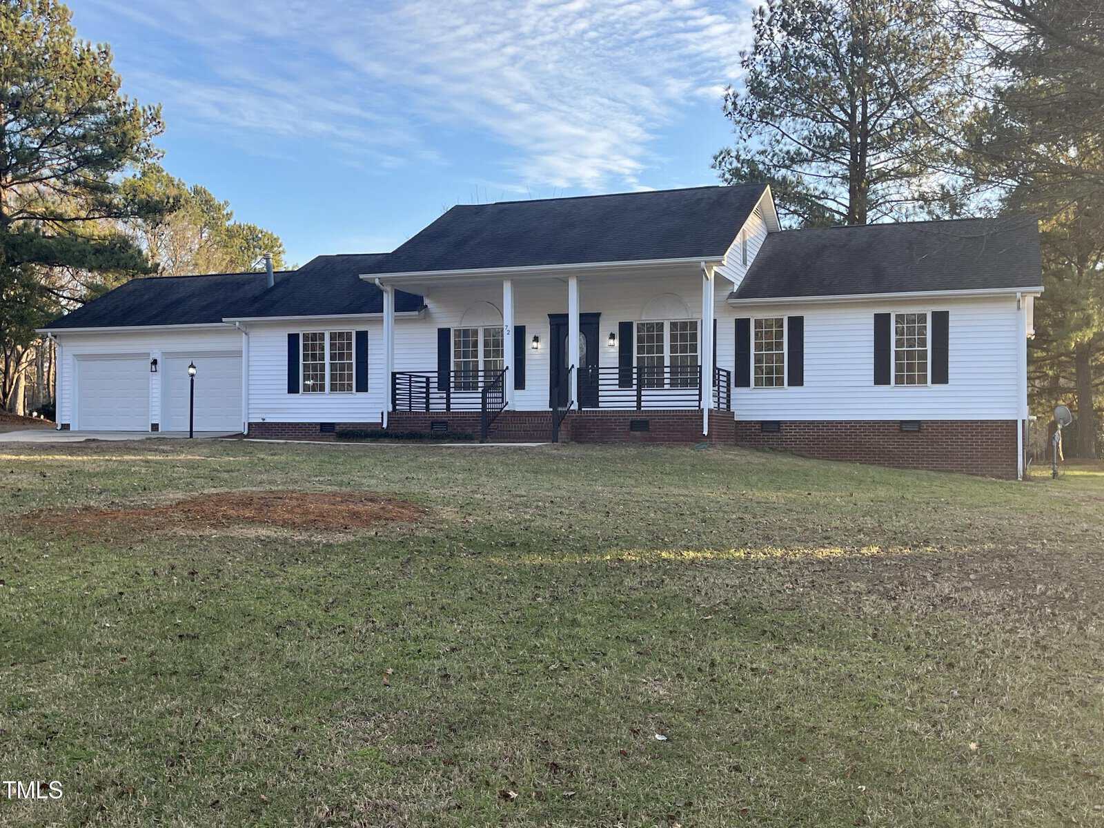 A single-story white house with a covered front porch, a two-car garage, and a grassy front yard with trees in the background.