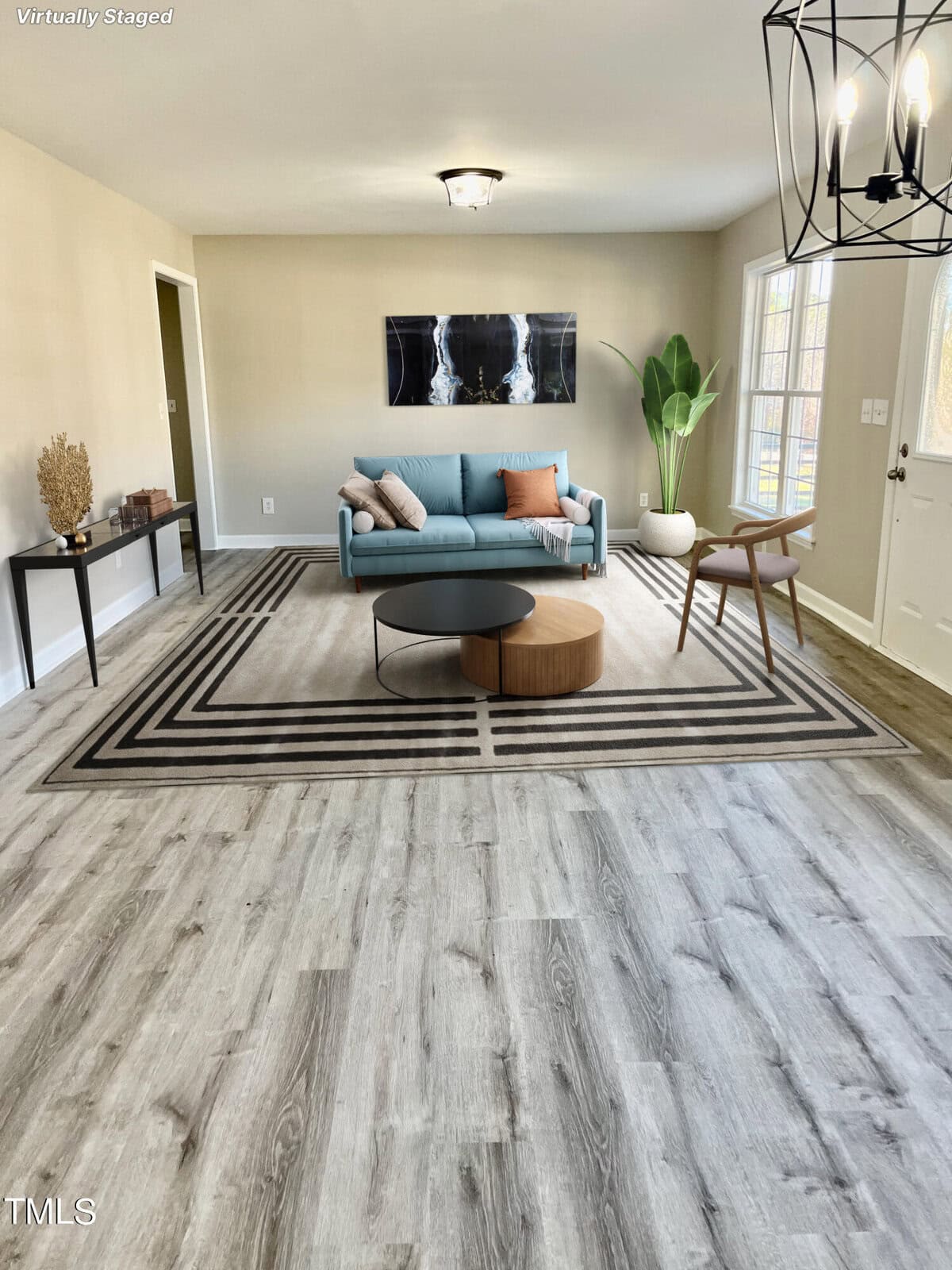 A modern living room with a two-tone sofa, a round coffee table, wood accent chairs, a geometric rug, and vinyl wood flooring, with a watermark indicating the image is virtually staged.
