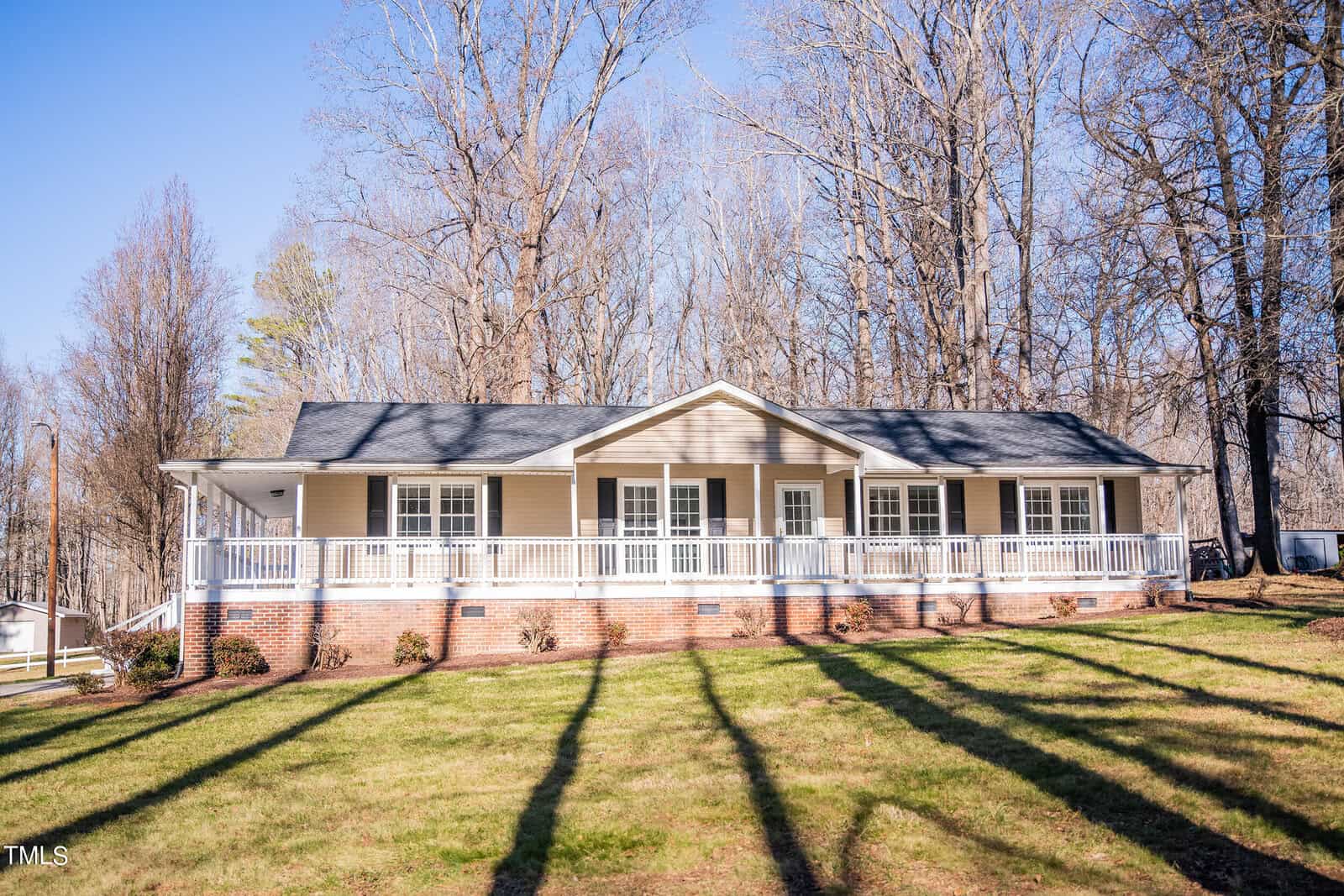 The single-story tan house at 2665 Gela Road in Oxford features a black roof and white trim, along with a long front porch. Surrounded by leafless trees under a clear blue sky, it boasts a well-kept grassy lawn in the foreground.