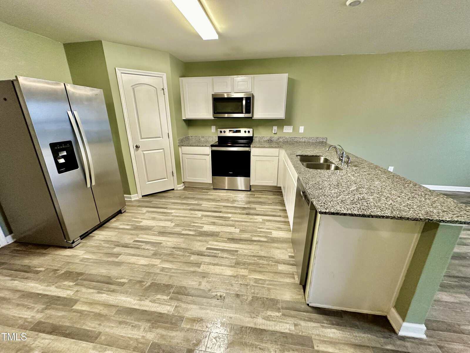 A modern kitchen featuring stainless steel appliances, granite countertops, and vinyl plank flooring.