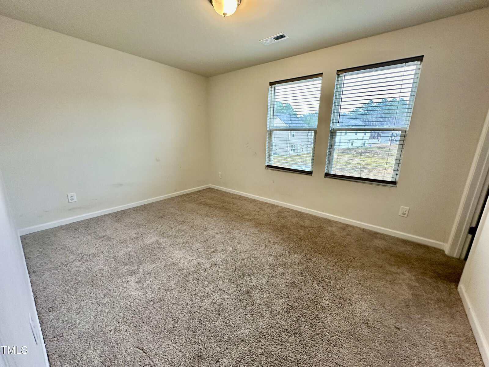 An empty room with beige carpeting, white walls, and two windows with blinds.