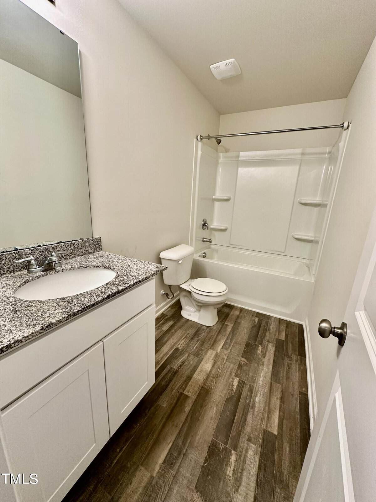A modern bathroom featuring a white shower unit, a single sink vanity with a granite countertop, and dark wood-look flooring.