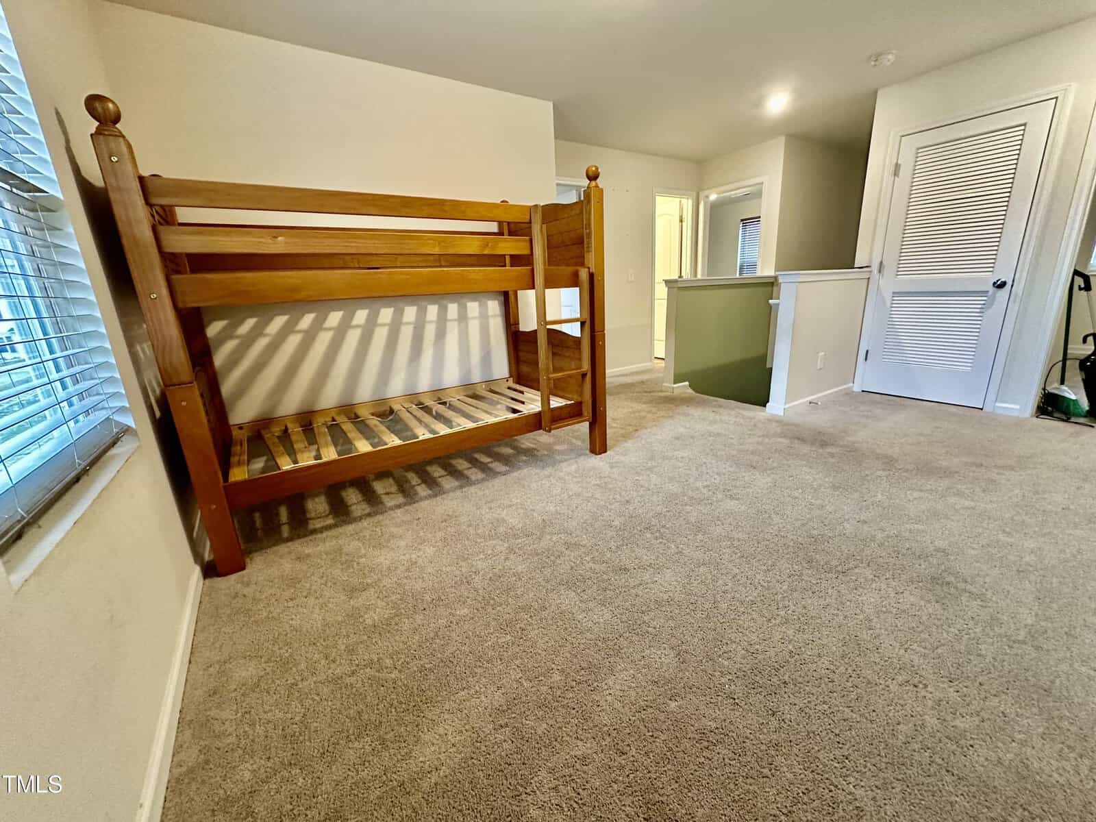 A wooden bunk bed with no mattresses is placed against the wall of an empty bedroom with beige carpeting and a closed closet door.