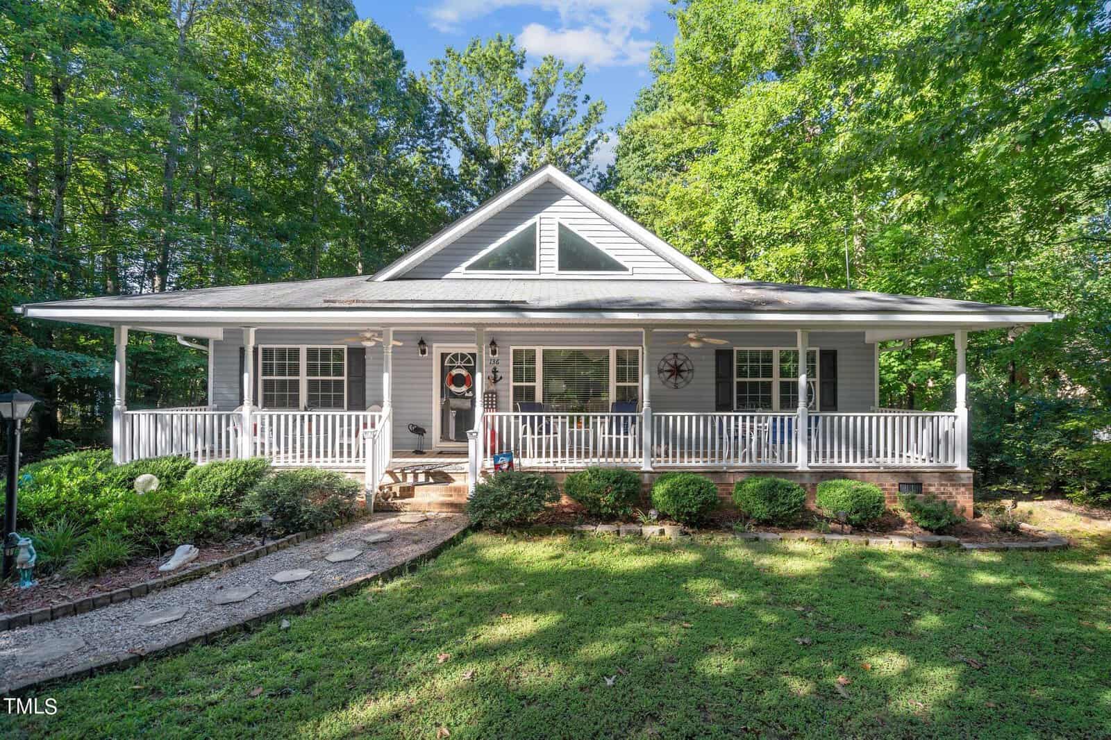 A single-story house at 136 Waters Edge Loop Rd, Henderson NC, with a covered front porch, surrounded by trees and adorned with decorative elements, set in a well-maintained lawn.
