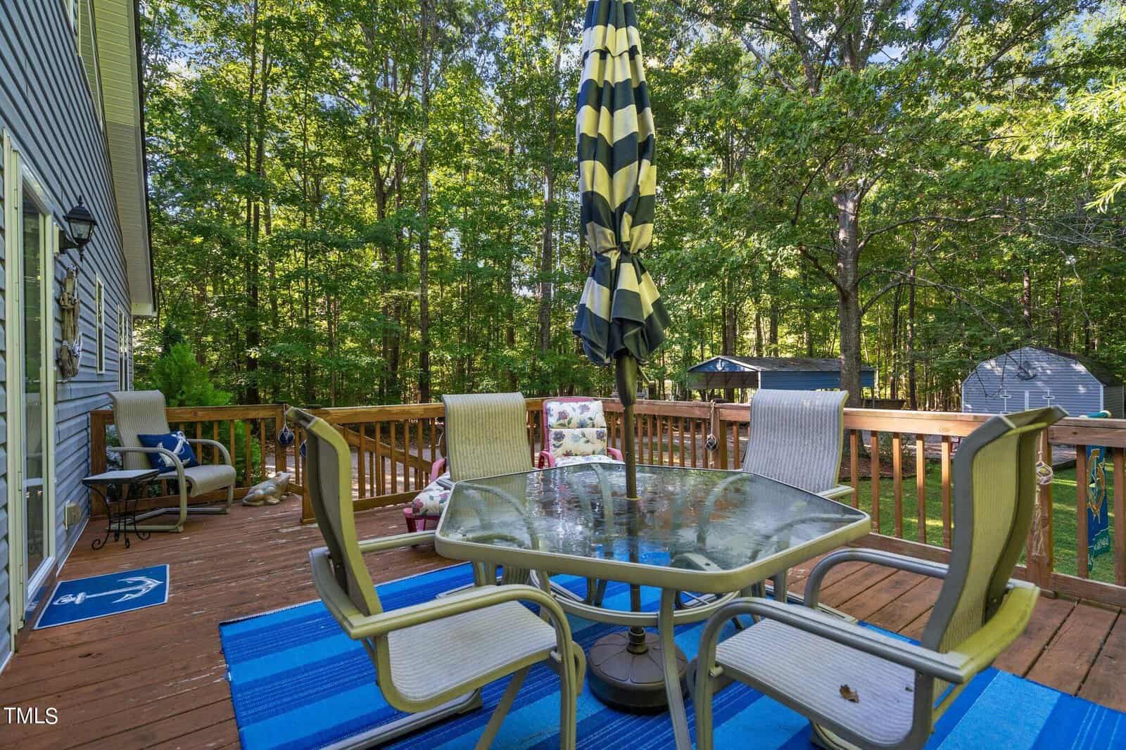 A spacious wooden deck surrounded by trees featuring outdoor furniture and an umbrella.