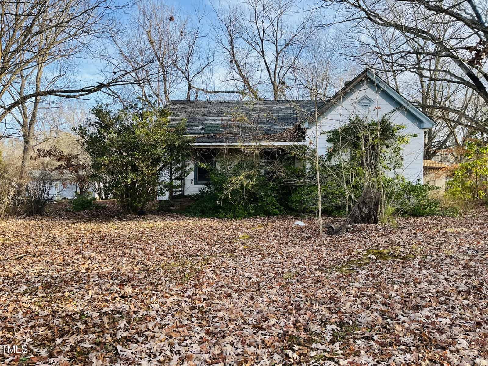 A small, white, weathered house on 210 King Street is surrounded by bare trees and bushes. The ground is covered in dry, fallen leaves, creating a rustic Oxford autumn atmosphere. The house features a gabled roof and appears secluded in its wooded area.