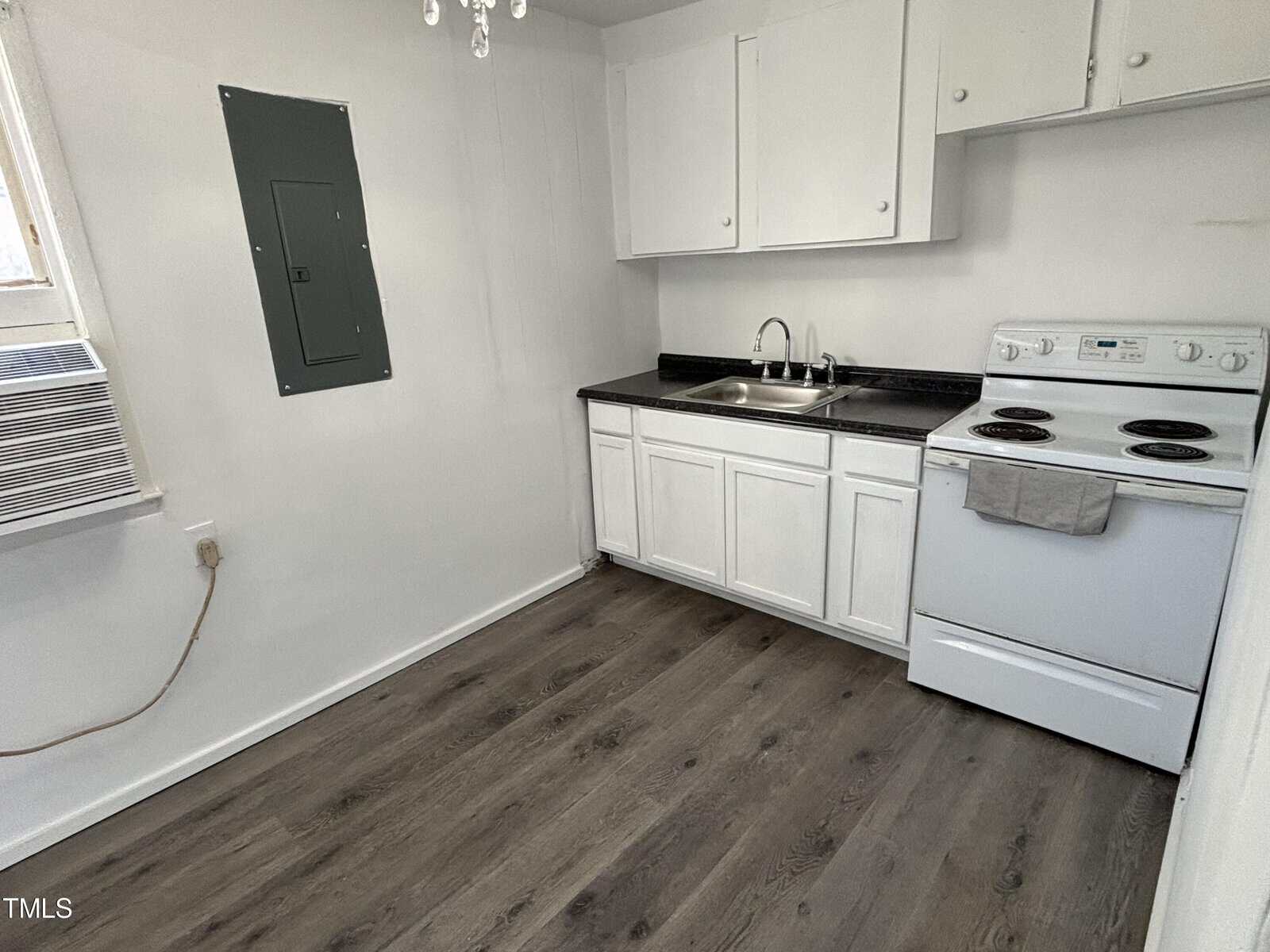 A small, functional kitchen with white cabinetry, black countertop, and white appliances including a stove and refrigerator. the floor is covered with gray laminate flooring.