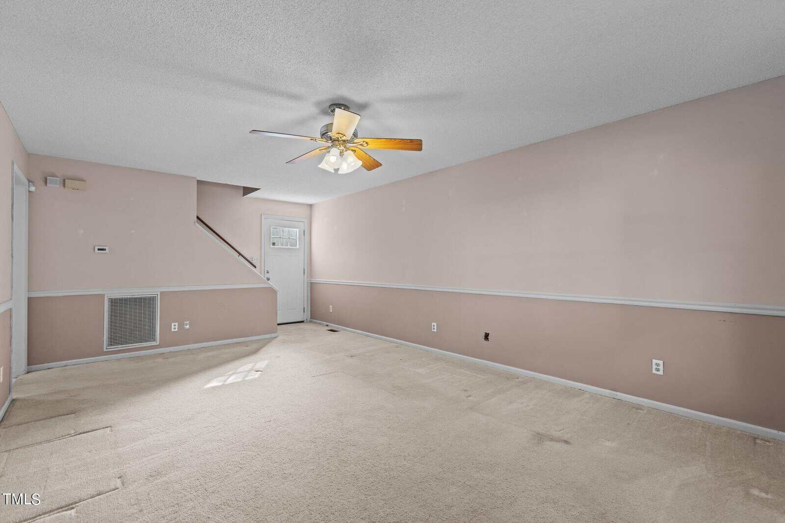An empty room with pink walls and beige carpet featuring a ceiling fan with light, several electrical outlets, and a white door.